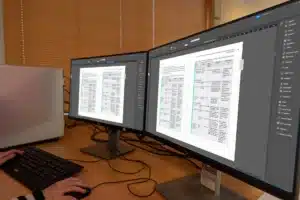 Grafisch boekomslag ontwerper werkt op twee beeldschermen aan de opmaak van een boekpagina in Adobe InDesign.