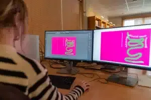 Grafisch boekomslag ontwerper maakt een kleurrijke boekomslag op twee beeldschermen met Adobe InDesign en Photoshop.