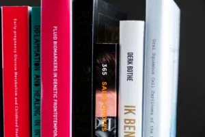 Close-up van meerdere boeken rechtop naast elkaar in een boekenkast, met gekleurde ruggen en titels in verschillende lettertypes.