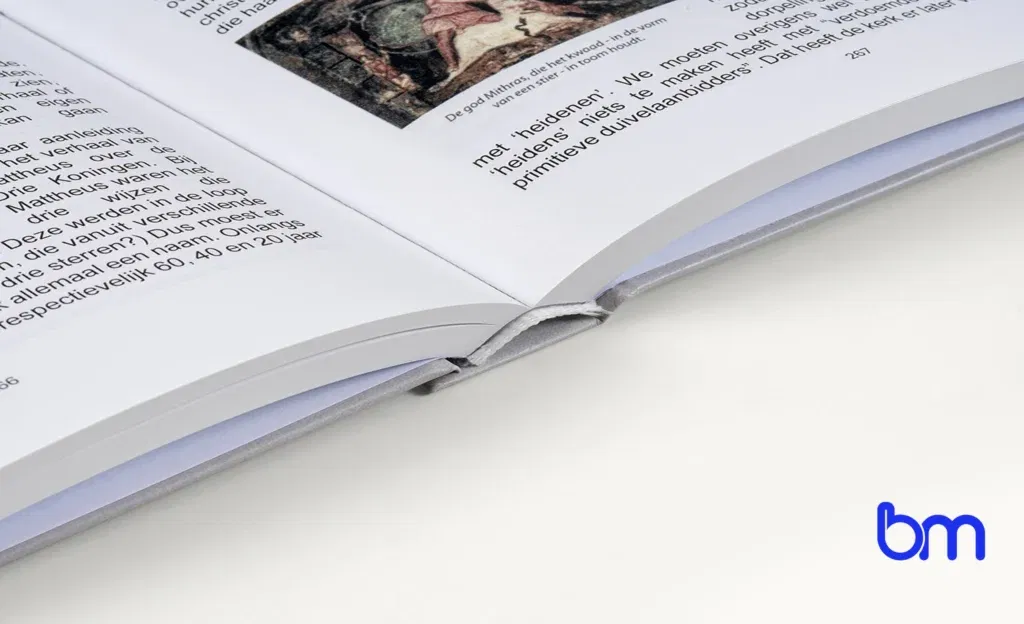 Open hardcoverboek met zichtbare rug en tekst op de pagina, Boekenmakers-logo rechtsonder op witte achtergrond.