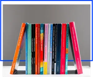 Kleurrijke rij softcover boeken rechtop tegen een grijze achtergrond.